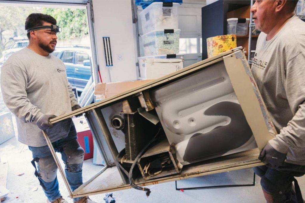 Technicians removing an old air conditioning unit for replacement.
