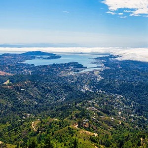 Aerial view of a lush, green landscape with hills and a bay under a partly cloudy sky.